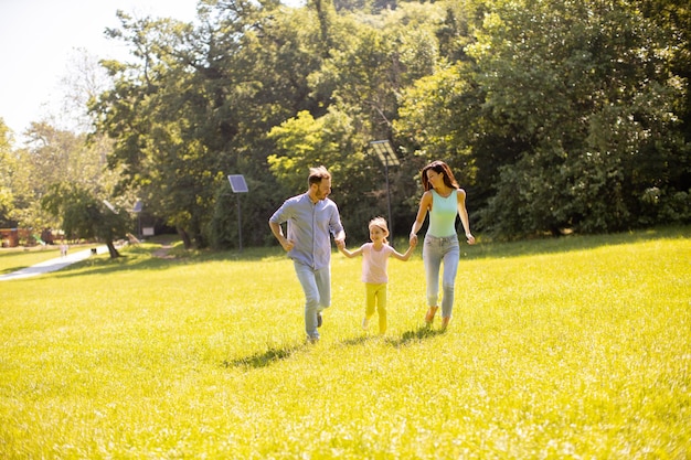 Familia joven feliz con linda hijita divirtiéndose en el parque en un día soleado