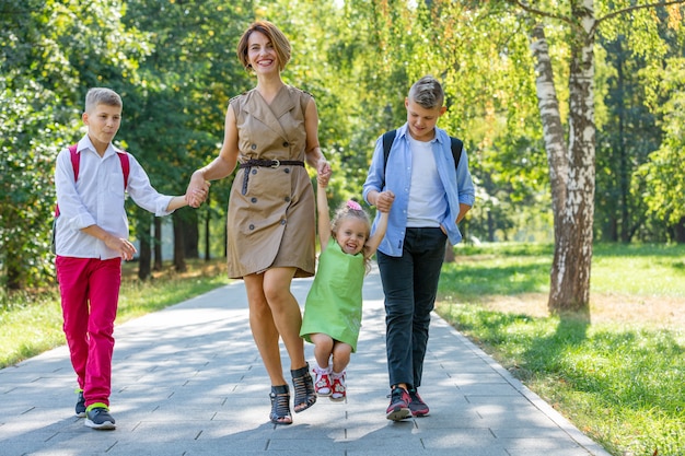 Familia joven feliz, madre con tres hijos caminando en el parque. Concepto de estilo de vida saludable