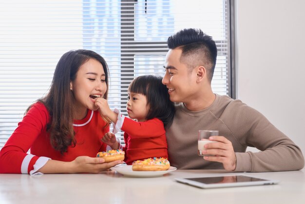 Familia joven feliz con niños disfrutando del desayuno en un soleado comedor blanco con una gran ventana con vista al jardín