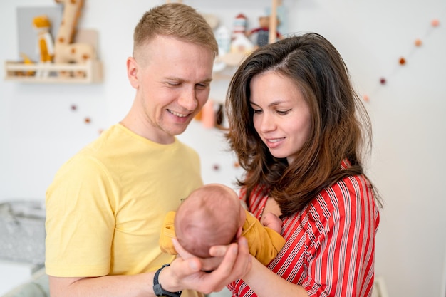Familia joven feliz con papá mamá y bebé recién nacido en la habitación del bebé