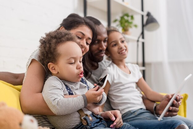 familia joven feliz pasando tiempo junto con dispositivos en el sofá