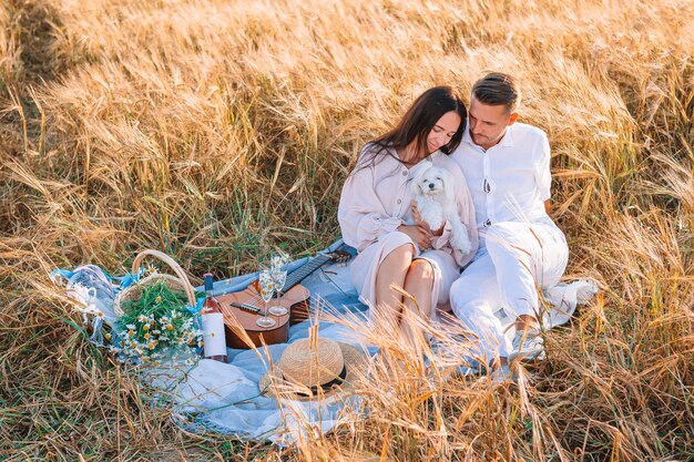 Familia joven feliz de picnic en campo de trigo amarillo