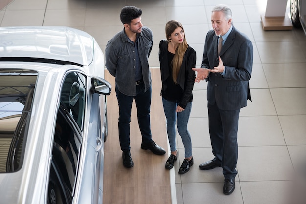 Familia joven feliz que habla con el vendedor y elige su nuevo automóvil en una sala de exposición