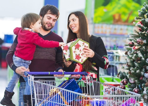 Familia joven feliz en el supermercado elige regalos para el nuevo año.