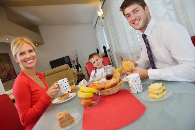 la familia joven feliz tiene un desayuno saludable en la cocina con detalles rojos en la luz brillante de la mañana