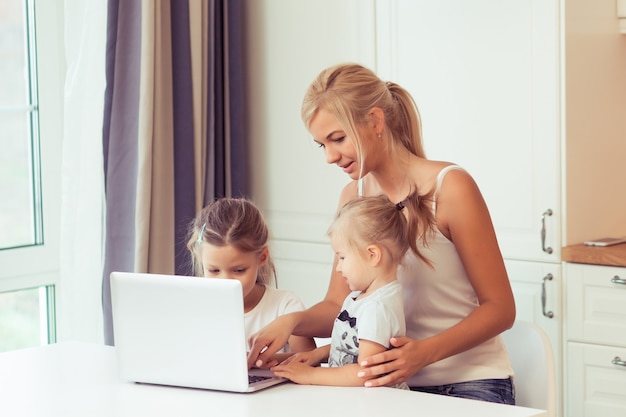 Familia joven feliz usando la computadora portátil mientras está sentado en la cocina en casa