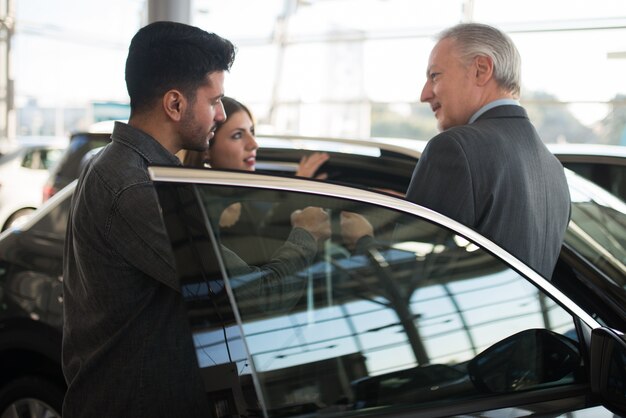 Familia joven hablando con el vendedor y eligiendo su nuevo coche en una sala de exposición