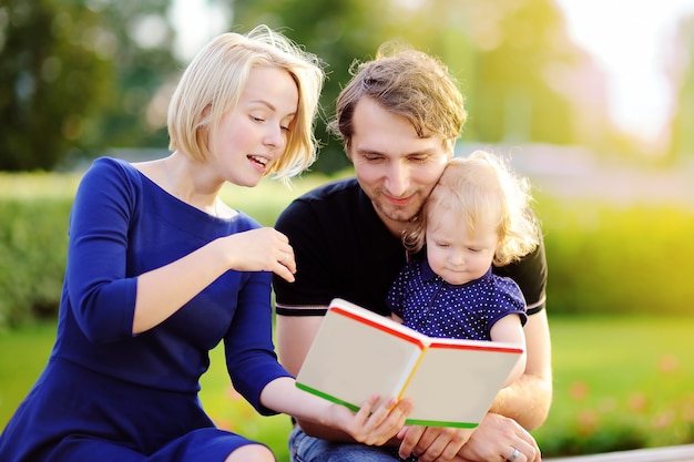 Familia joven leyendo libro de papel juntos al aire libre