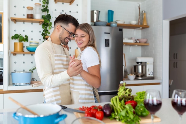 Familia joven muy contenta divirtiéndose en la cocina moderna bailando y riendo feliz joven esposa y esposo moviéndose con su música favorita disfrutando del tiempo libre cocinando juntos una cita romántica