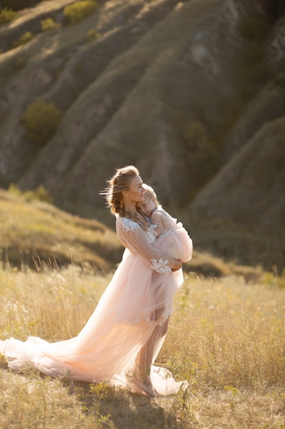 Una familia joven en la naturaleza con vestidos idénticos. hermosa joven madre sostiene a su hija en sus brazos.