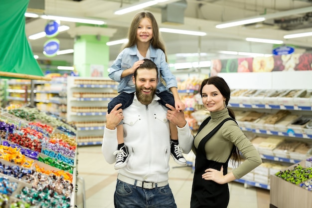 Foto una familia joven con una niña pequeña elige dulces y chocolate en una gran tienda, supermercado.
