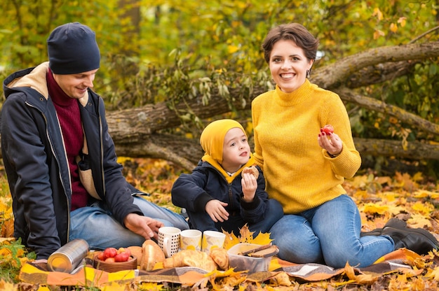 Una familia joven con un niño pequeño haciendo un picnic en la naturaleza otoñal