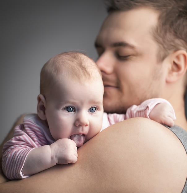 Familia joven. El padre sostiene a la hija en las manos. El hombre no está afeitado y sonríe. Niña con lengua fuera. Foto a color