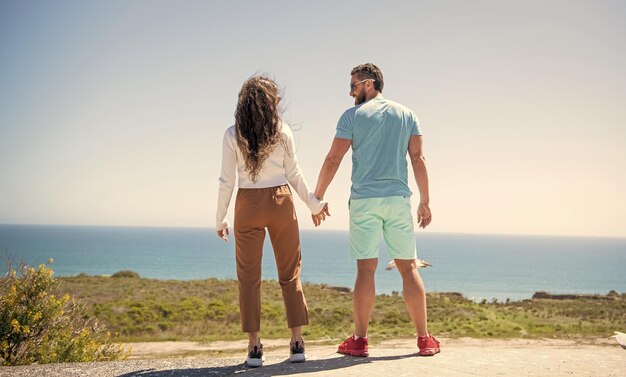 Familia joven pareja tomados de la mano mirando el agua de mar desde la libertad superior