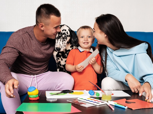 Familia joven con un perro hacer trabajo creativo en casa, pintar y esculpir con plastilina