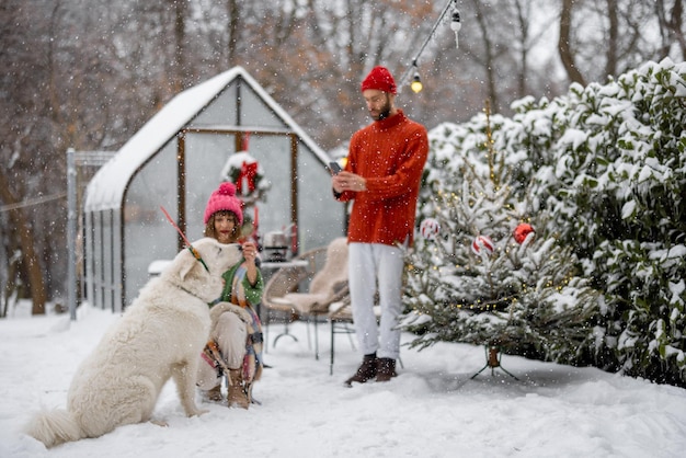 Familia joven con un perro en el patio cubierto de nieve durante las vacaciones de invierno