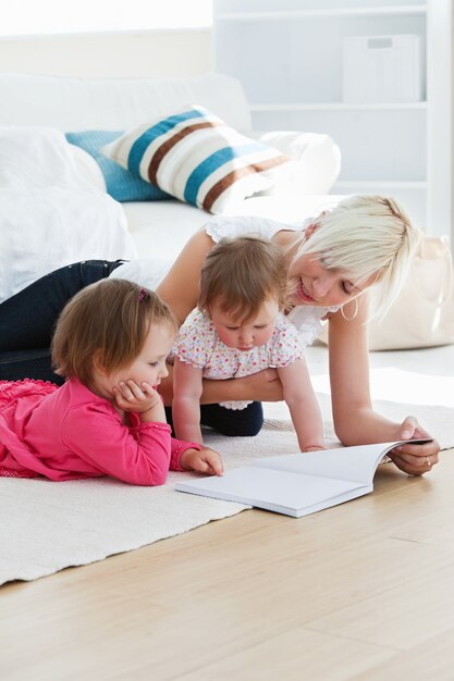 Familia joven positiva leyendo un libro en el piso