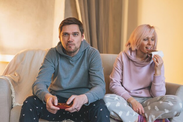 Familia joven en ropa de casa jugando videojuegos en el sofá en la sala de estar