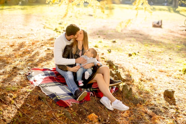 Familia joven sentada en el suelo en el parque de otoño