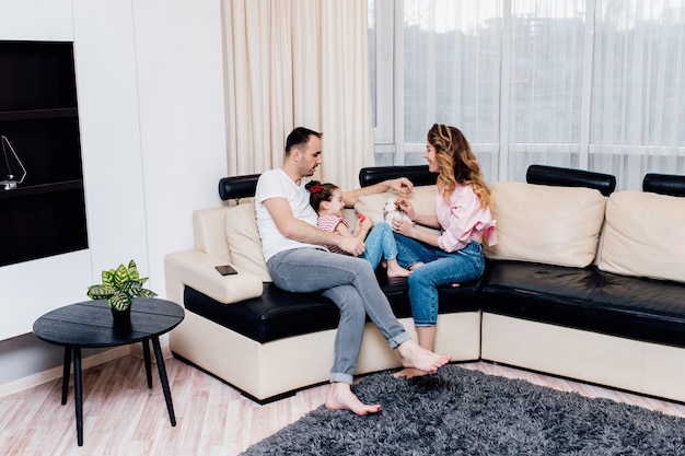 Familia joven en el sofá en la sala de estar, padre, hija y madre jugando en casa.