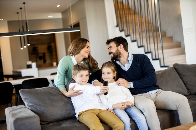 Familia joven sonriente viendo la televisión juntos en el sofá de la sala de estar