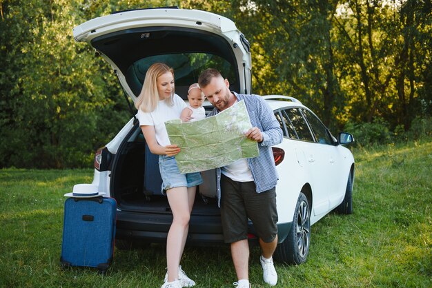 Familia joven tres personas vestidas de blanco tienen comida campestre. Hermosos padres e hija viajan en coche durante las vacaciones de verano. Escena en el parque