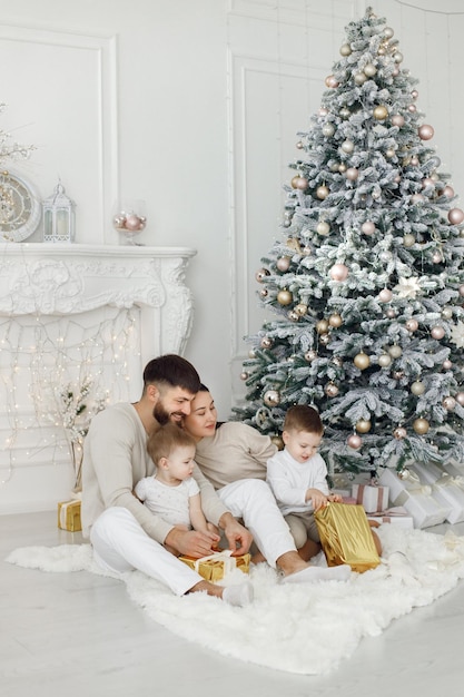 Familia joven vestida de blanco sentada cerca del árbol de Navidad