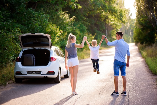 Familia joven viaja en coche. Papá, mamá e hijo pequeño se toman un descanso de conducir un automóvil y caminan.