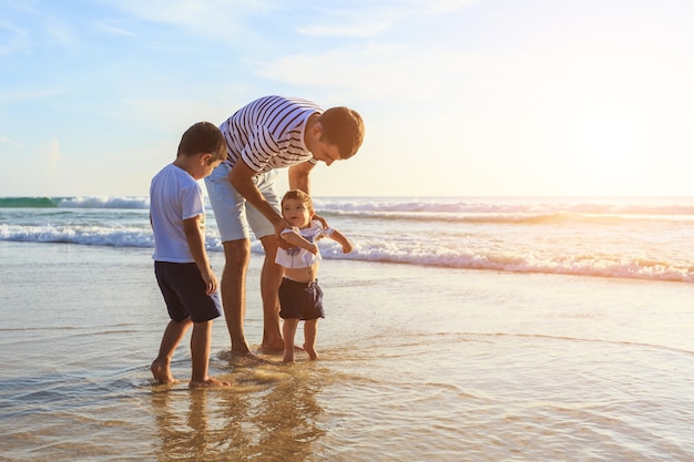 Foto familia jugando con el hijo en la playa en el atardecer