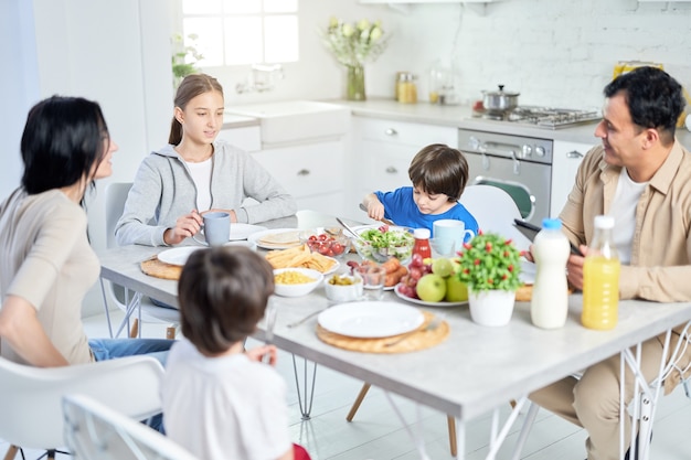 Família latina feliz desfrutando a refeição juntos, sentados à mesa na cozinha em casa. Infância, conceito de alimentação