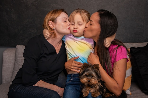 Foto familia lesbiana y su hija sentada en el sofá con su perro mascota