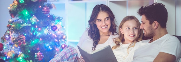 La familia leyó el libro cerca del árbol de navidad por la noche.