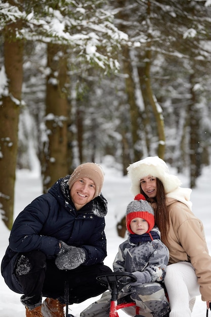 Familia de madre, padre e hijo divirtiéndose en madera de invierno nevada con perro mascota alegre