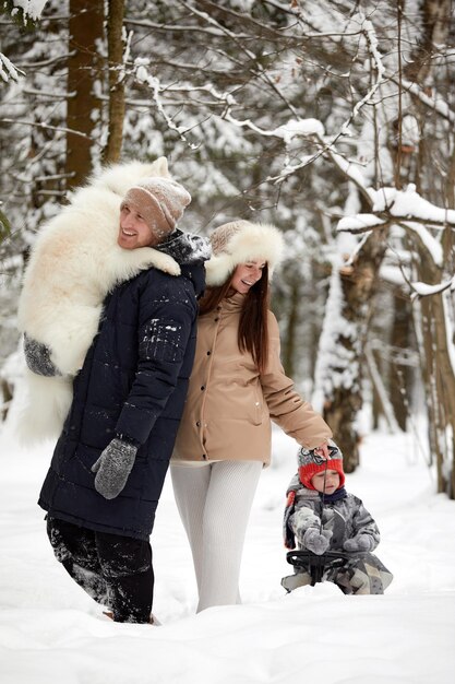 Familia de madre, padre e hijo divirtiéndose en madera de invierno nevada con perro mascota alegre