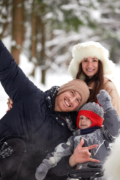 Familia de madre, padre e hijo divirtiéndose en madera de invierno nevada con perro mascota alegre