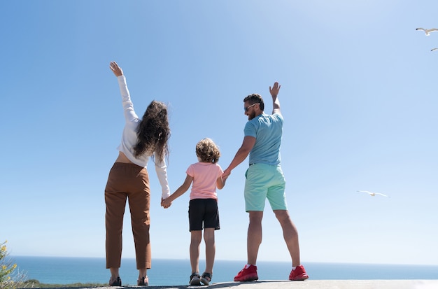 Familia de madre, padre y niño mirando en el futuro tomados de la mano en verano, vista posterior, adopción.