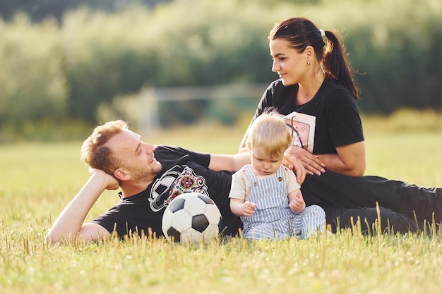 Familia de madre padre y niño pequeño está en el campo verde con la pelota de fútbol