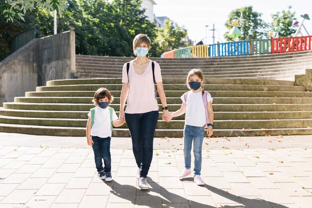 Familia de una madre con sus dos hijos caucásicos yendo a la escuela al comienzo del año escolar con máscaras debido a la pandemia del coronavirus covid19