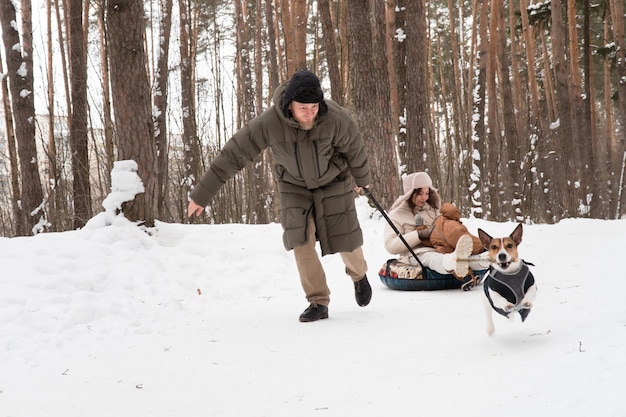 Família (mãe, pai e bebê) andando na floresta de inverno com cachorro jack russell terrier