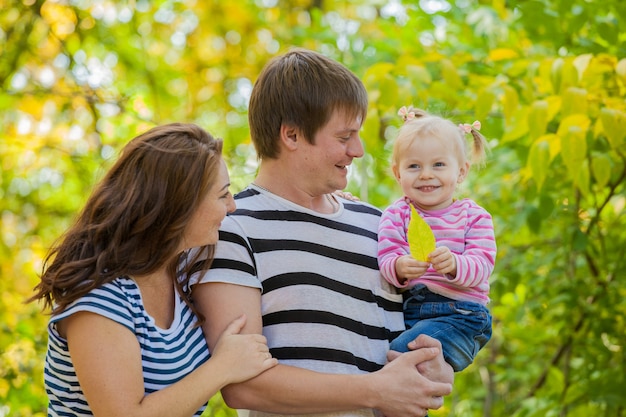 Familia Mamá, papá e hija a dar un paseo por el parque en otoño. El niño está en las manos seguras del padre.