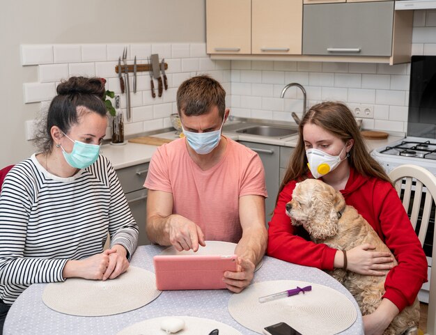 Foto familia en máscaras protectoras viendo noticias impactantes en una tableta en casa