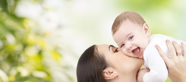 família, maternidade, filhos, paternidade e conceito de pessoas - mãe feliz beijando seu bebê sobre fundo verde natural