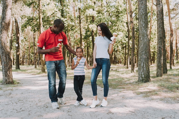 Foto familia mixta feliz comiendo helado en el bosque.