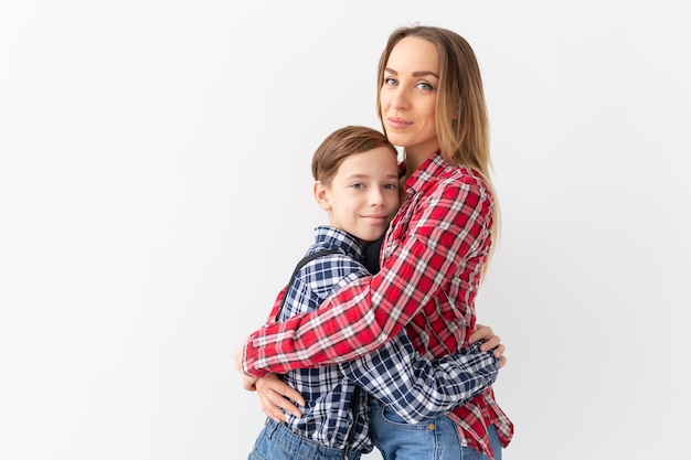 Família, moda e conceito de dia das mães - menino adolescente abraçando sua mãe no fundo branco.