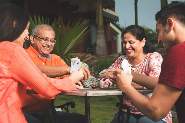 Familia moderna asiática india jugando a las cartas y divirtiéndose mientras está sentado en el césped, al aire libre