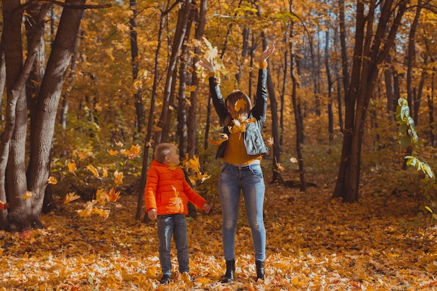 Família monoparental brincando com folhas de outono no parque. Feliz mãe e filho jogam folhas de outono no parque de outono.