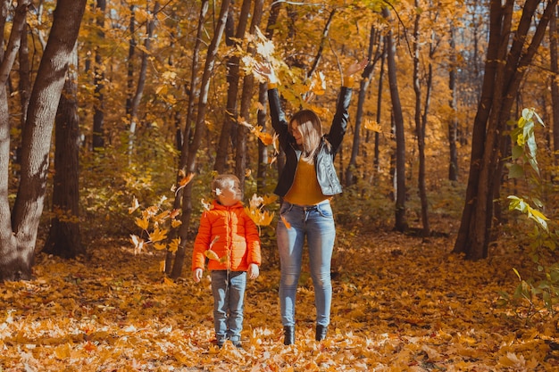 Família monoparental brincando com folhas de outono no parque. Feliz mãe e filho jogam folhas de outono no parque de outono.