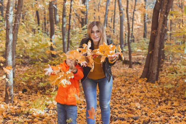 Familia monoparental jugando con hojas de otoño en el parque mamá e hijo felices tiran hojas de otoño en