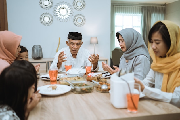 Família muçulmana asiática feliz rezando antes de fazer a refeição iftar durante o jejum do ramadã