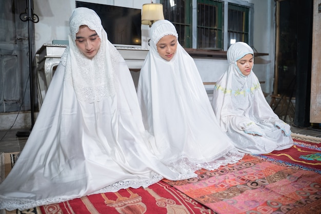 Família muçulmana asiática orando jamaah juntos em casa. sholat ou salah vestindo branco e hijab